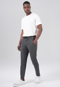 Gray jogger pants made of soft fabric, featuring a drawstring waist, side pockets, and tapered legs, paired with a plain white t-shirt and white sneakers.