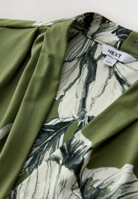 Žalia palaidinė su minkšta, lygiu audiniu. Puošta gėlių raštu su juodomis kontūromis ir V formos iškirpte. Matoma prekės ženklo etiketė viduje.