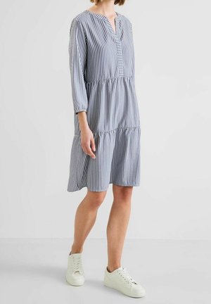 Femme portant une robe bleu et blanc à rayures verticales mi-longue avec des manches trois-quarts et des baskets blanches à lacets.