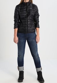 Svart puffjacka med dragkedja fram, med horisontell quiltning, kombinerad med trasiga blåjeans och svarta snörstövlar.