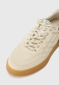 Baskets rétro couleur crème avec un upper en cuir lisse perforé, des lacets ronds et une semelle en caoutchouc gomme. Logo subtil sur la languette.