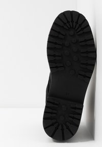 Suela de bota negra con surcos profundos y patrones hexagonales, fabricada con un material de goma plana y duradera. Talla marcada como 37.