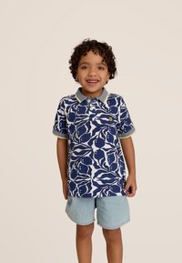 Marineblauwe en witte gestreepte polo met een grijze kraag en gele accenten, gecombineerd met lichte denim shorts. Korte mouwen en knopen aanwezig.