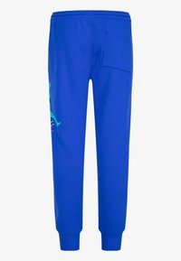 Blå joggebukser laget av mykt stoff, med et brodert logo i kontrasterende farger og en baklomme med en avrundet klaff.