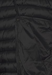 Schwarze Steppweste mit gesteppten Abschnitten, glatter Außenseite und großer Seitentasche. Das Material wirkt leicht und isoliert.