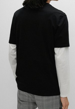 Black short-sleeve t-shirt layered over a white long-sleeve shirt, set against a plain background, with visible stitching details.