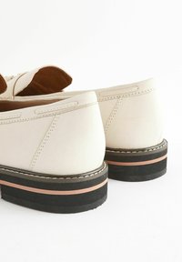 Vaaleanbeige kengät, jotka on valmistettu sileästä nahasta ja niillä on pyöreä muoto. Pohjassa on kerroksellinen design mustana ja persikanvärisenä, jossa on ompeluyksityiskohtia.