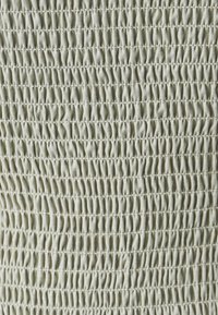 Tissu beige clair avec des points de smocking froncés uniformément espacés formant un motif texturé et plissé.