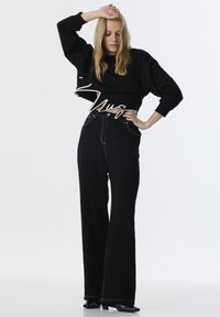 Sudadera corta negra con dobladillo curvado, combinada con jeans anchos de tiro alto en negro que presentan costuras en contraste y bolsillos frontales.