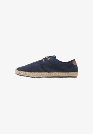 Espadrille en toile bleu marine avec une finition texturée, semelle en jute, accent tan contrastant au talon et fermeture à lacets.