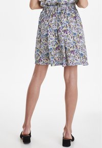 Abito floreale con un motivo multicolore in tonalità di blu, viola e verde. Vita elastica e tessuto leggero. Scarpe nere.