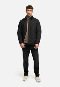 Chaqueta de quilt negra con cuello, llevada sobre un suéter beige. Combinada con pantalones vaqueros negros y zapatillas de colores claros. Diseño simple, sin patrones.