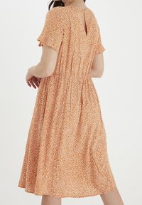 Pomarańczowa sukienka w kwiatowy wzór z krótkimi rękawami, o długości midi, z gumką w pasie oraz dekoltem w kształcie łezki z tyłu, wykonana z lekkiego materiału.