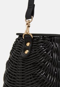 Czarna pleciona torebka o fakturowanej powierzchni, wyposażona w złocisty zatrzask i czarny skórzany pasek. Charakterystyczny zaokrąglony kształt i ozdoby w postaci nitów.
