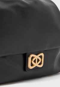Borsa in pelle nera con una texture liscia e una chiusura in metallo dorato con design intrecciato. Presenta una leggera lucentezza e uno stile minimalista.
