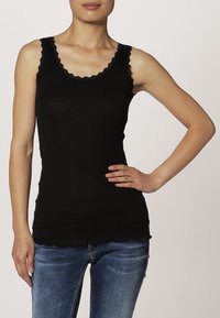 Zwarte geribbelde tanktop met golvende kantafwerking langs de halslijn en armgaten, fitted ontwerp, gedragen met blauwe spijkerbroek.