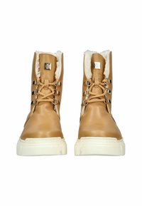 Botas de cuero sintético marrón con forro de piel sintética blanca, que presentan un acabado suave, punta redondeada, suela de goma blanca en contraste y detalles decorativos de metal.
