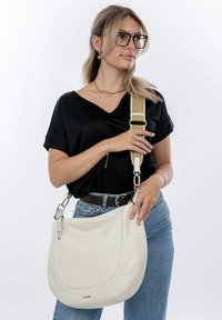 Borsa a mano in pelle bianca con forma curva, dotata di una tracolla regolabile beige e dettagli in metallo argentato. Texture liscia e cuciture minime.