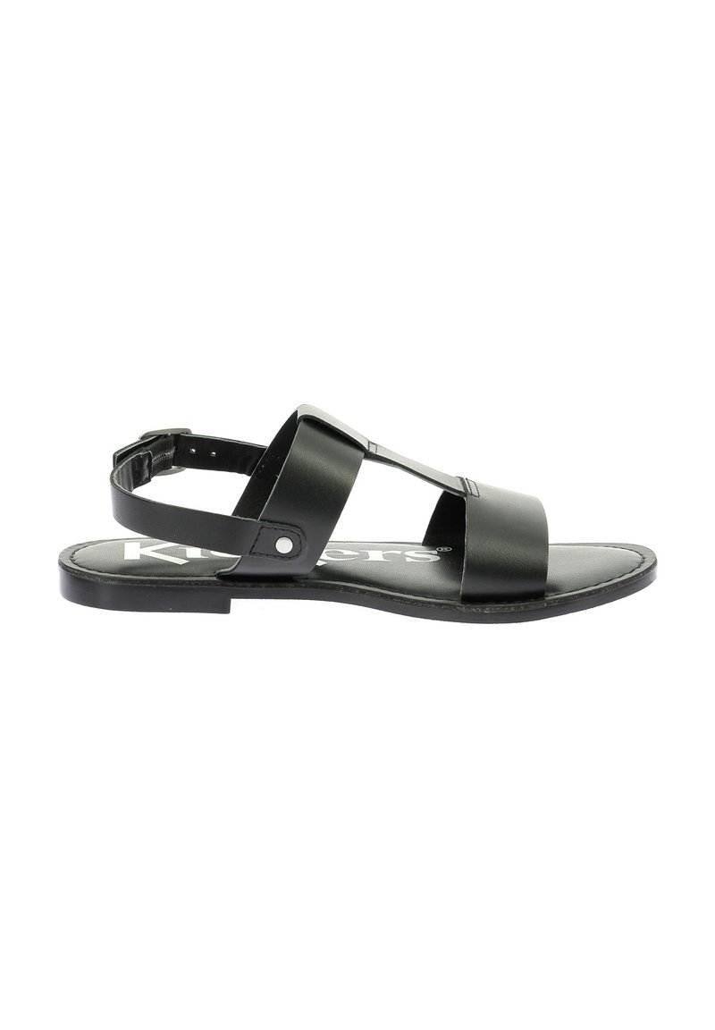 Sandalia de cuero negro con suela plana, que presenta dos correas anchas sobre el pie y una correa ajustable en el tobillo. Diseño simple y minimalista.