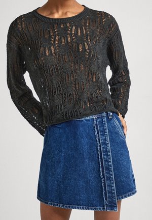 Osoba ubrana w czarny dzianinowy top z długim rękawem i ażurowym wzorem oraz niebieską dżinsową mini spódniczkę z wykończeniem z postrzępionym brzegiem.