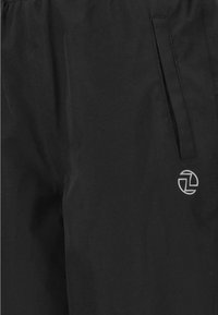 Schwarze Sporthose aus leichtem Material, mit einer Seitentasche und einem runden, silbernen Logo im unteren Bereich.