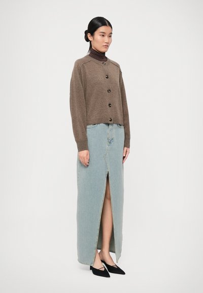 Brown knit cardigan with button closure paired with a light blue denim maxi skirt featuring a front slit, complemented by black pointed shoes.