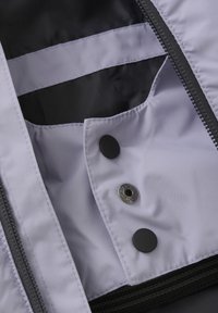 Ljuslila jacka med svart foder. Har tryckknappar och en dold ficka. Texturerad yta och kraftig dragkedjestängning.