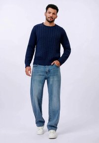Marinblå ribbad stickad tröja med rund halsringning, som kombineras med ljusblå raka jeans och vita sneakers. Enkel design utan synliga mönster.