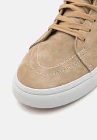 Semišové béžové tenisky s bílou gumovou podrážkou, kontrastním bílým prošíváním a plochými tkaničkami. Kulatá špička s minimalistickým designem.