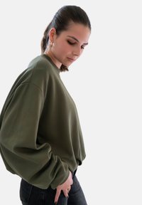 Oversized olijfgroen sweatshirt met een ronde halslijn en verlaagde schouders, gemaakt van een zachte, gestructureerde stof. Gecombineerd met zwarte jeans.