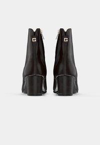 Botine din piele neagră, cu toc pătrat, închidere cu fermoar și un detaliu logo proeminent pe spate. Textură netedă și design elegant.
