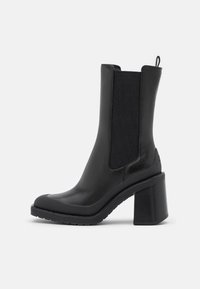 Černá kožená kotníková bota s robustním podpatkem, disponující elastickými postranními panely, hladkým povrchem a zaobleným tvarem špičky.