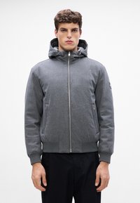 Siva zip-up jakna s kapuco, ki ima gladko teksturo, dva stranska žepa ter rebrastim manšetami in robom. Preprost, čist dizajn.