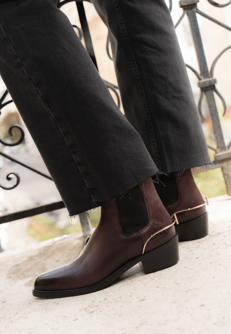 Bruna läderankelboots med spetsig tå, elastiska sidor och ett guldaccentuerat band vid hälen. I kombination med svarta vida byxor.