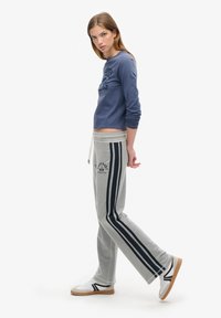 Niebieska bluzka z długim rękawem z napisem, w połączeniu z szarymi spodniami dresowymi z bocznymi paskami i akcentem logo, uzupełnione białymi sneakersami.