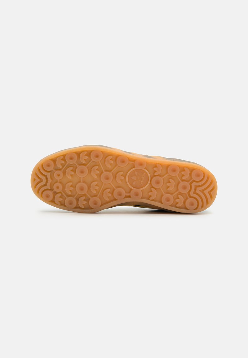Sole in gomma color sabbia con motivi di trazione circolari e superficie texturizzata. Presenta un logo al centro e bordi ondulati nel design.