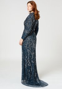 Robe longue bleu marine à manches longues avec des détails en perles argentées élaborés et une traîne fluide, présentant une silhouette ajustée et une texture en dentelle.