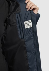 Tengerész kék puffertakó belseje, varrott textúrával, sima anyaggal és egy címkével, amely azt írja: "Egy meleg ölelés, amely szövetből készült."