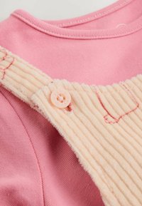 Roze geribde baby-broekjes met een bijpassende roze knop die vastzit aan een zachte, crèmekleurige corduroy band.
