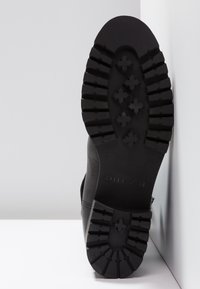 Suela de bota de cuero negro con banda de goma texturizada, que presenta patrones en cruz y una marca. Tamaño 37 indicado en el lateral.