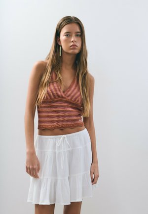 Haut en crochet à bretelles dans des teintes de rose chaud et d'orange, associé à une jupe blanche à volants avec une taille élastique et un cordon de serrage.