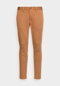 Pantalon chino beige à coupe slim, doté d'une texture lisse, de passants pour ceinture et d'une fermeture à bouton unique. Aucun motif ou accent visible.