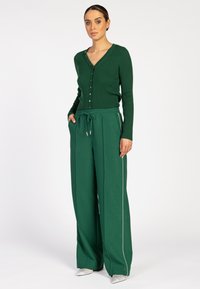 Groene geribbelde gebreide cardigan met V-hals en knoopsluiting, gecombineerd met groene trekkoordbroeken met zijpiping en een relaxte pasvorm.