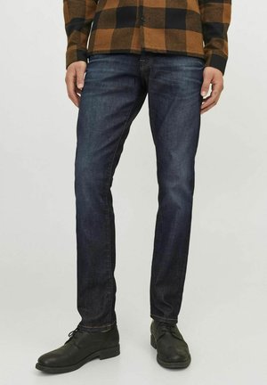 Jeans de mezclilla azul oscuro con un corte slim, con costuras en contraste y un diseño clásico de cinco bolsillos, combinados con zapatos negros.