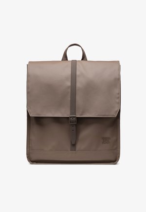 Brun, slidstærk stof rygsæk med klaplukning, justerbar rem og et brandlogo i det nederste hjørne. Glat, minimalistisk design.