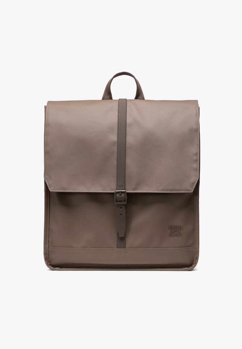 Brun, hållbar tygryggsäck med klaffstängning, justerbar rem och en märkeslogotyp i nedre hörnet. Slät, minimalistisk design.