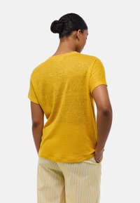 T-shirt jaune à manches courtes en tissu texturé, présentant une coupe décontractée et un col rond. Un pantalon rayé est visible en bas.