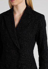 Zwarte gestructureerde blazer met bloempatronen, een pieklapel en een dubbelgebouwde ontwerp met opvallende knopen.