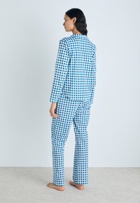 Conjunto de pijama em azul e branco com padrões xadrez, composto por mangas longas e calças, apresentando um corte relaxado e tecido suave. Os detalhes mostram uma cobertura de padrão consistente.