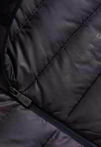 Svart quiltad jacka med dragkedja, gjord av slät, lättviktig tyg med en subtil glans och "Sail Racing"-logotyp i en kontrasterande nyans.